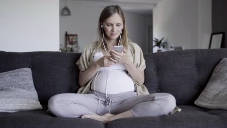Smiling-pregnant-woman-choosing-and-listening-to-music